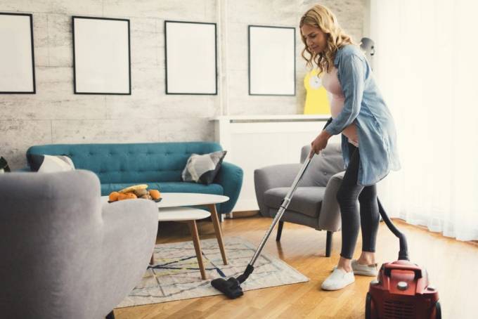 This image shows that a blond women do cleaning in the room using vacuum cleaner